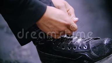 在黑暗的地板背景下，双手将鞋带系在冰球鞋上
