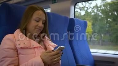 年轻漂亮的女人坐在<strong>火车车厢</strong>的乘客座位上，掏出一个电话来写一条信息。 长发，粉红色
