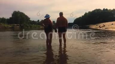 成熟的夫妻-拥抱俯瞰河流。 一对漂亮的老人在水边。 快乐老人牵着手