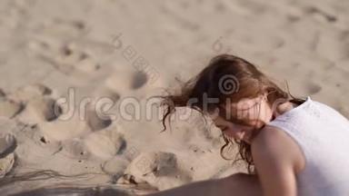 一个女孩正在用手指倒沙子。 女孩手`沙子。 坐在沙滩上的女孩。 快乐的女孩