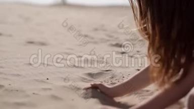 一个女孩正在用手指倒沙子。 女孩手`沙子。 坐在沙滩上的女孩。 快乐的女孩