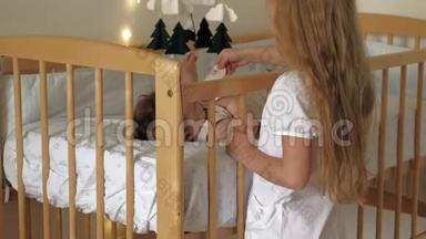 女孩学龄前女孩和一个孩子站在婴儿床旁，给她<strong>舒缓</strong>。 照顾小妹妹