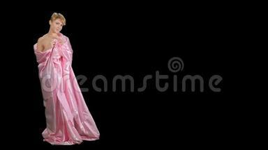 穿着粉红色缎子<strong>床单</strong>的迷人女孩在黑色背景下为相机摆姿势
