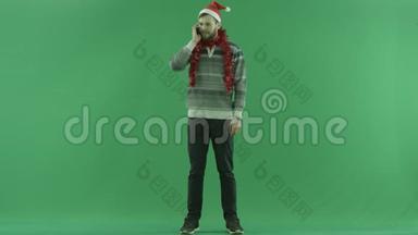 年轻的大胡子，快乐的男人在圣诞节谈论智能手机，绿色的关键背景