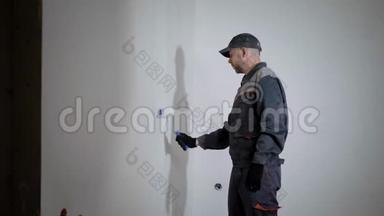 专业油漆工穿着工作制服，帽子是用白色滚筒粉刷墙壁，侧视