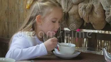 可爱的小女孩在咖啡馆喝茶。 清淡的早餐。 小白种人女孩在咖啡馆喝茶。
