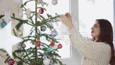 一位红发的年轻女子用窗边的玩具装饰圣诞树。慢动作。3840x2160