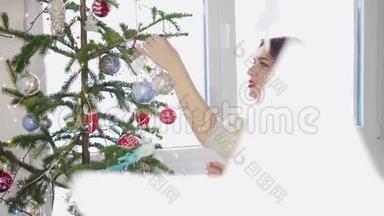 年轻漂亮的女人在窗边用玩具装饰圣诞树。 慢动作。 3840x2160