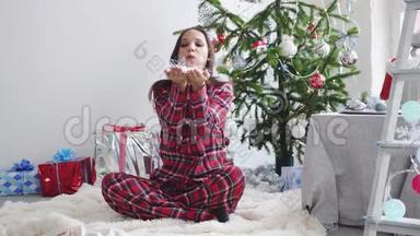 年轻<strong>漂亮</strong>的女人在冷杉圣诞<strong>树上</strong>吹着纸屑，坐在地毯和工作室的窗户上。 慢动作。 3840x2160