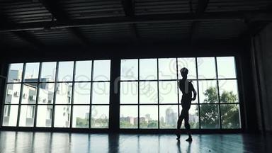 一位芭蕾舞演员的剪影，男演员在一扇大窗户的背景下跳舞。 舞蹈演员优雅地在舞蹈中翩翩起舞
