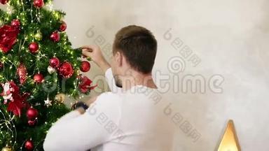年轻人拿着一个球挂在一棵人造圣诞树上的背面。 在家装饰圣诞树。 慢动作