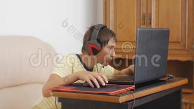 使用笔记本电脑的青少年。 带着耳机的青少年男孩用电脑游戏鼠标粘在笔记本屏幕上。