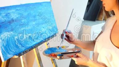 一位年轻的女<strong>艺术</strong>家在她的车间里用蓝色油画颜料在画布上作画。