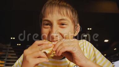 青少年吃快餐。 在快餐店里，一个饥饿的少年咬芝士汉堡的特写镜头。