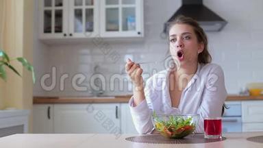 一个女人在美丽的晨光中拿着一盘新鲜的绿色沙拉。 她`拿着叉子