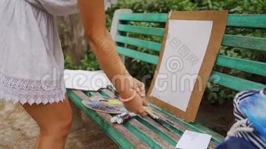 女孩艺术家准备纸调色板和油漆刷在公园的风景画与一个小池塘4k