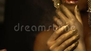 <strong>化妆</strong>师<strong>正在</strong>把金色的喷雾喷在美丽迷人的非洲女人的身上，她的嘴唇是红色的光泽
