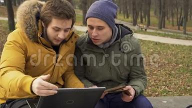 学生们使用笔记本电脑和平板电脑坐在公园的长凳上