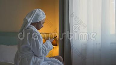 穿<strong>白色浴袍</strong>的年轻女子坐在酒店的床上