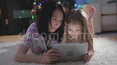 一家人的母亲和女儿在躺在地上数字平板电脑上的礼物。 圣诞节。
