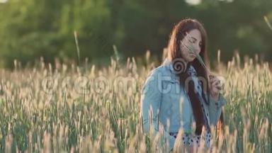 年轻漂亮的女孩，一头乌黑的长发，在一片麦田里，在绿色的小穗中享受着大自然和夏天。 自由