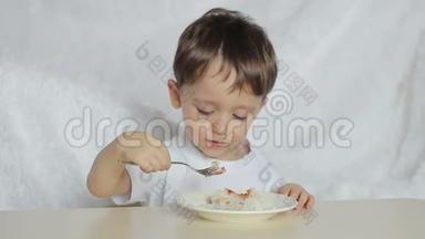 这个男孩高兴地用勺子从盘子里吃汤，<strong>特写</strong>。 运动相机滑块。 一个男孩坐在那儿<strong>吃饭</strong>