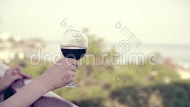 女子手捧一杯红酒，在酒庄露台上观海.. 女孩慢慢地摇晃着杯子