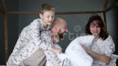 父母带着一个孩子在卧室里穿着相同的睡衣，抱着枕头在床上胡闹