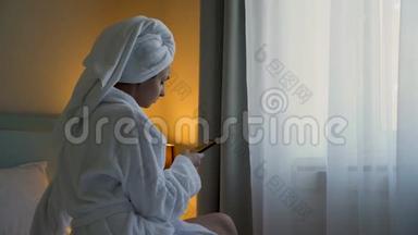 穿白色浴袍的年轻女子坐在酒店的床上