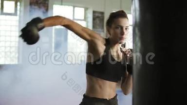 年轻的白种人女<strong>拳击</strong>手在健身房里用手套和烟一起<strong>打拳击</strong>袋。 严格的电力训练