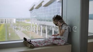 在机场窗口附近的孩子在平板电脑上玩游戏，等待飞行时间