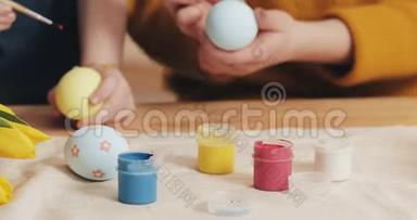 妈妈和女儿用手把复活节彩<strong>蛋</strong>用颜色和刷子贴紧。 五颜六色的复活节彩<strong>蛋</strong>。 筹备工作