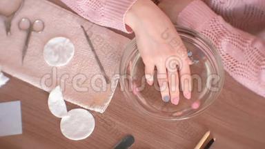 家里的手法。 女人把手伸进一碗水里。 手特写，美甲工具<strong>放在桌面</strong>上.. 上景。