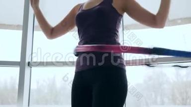 健身室，身材魁梧的女孩在大型窗户的背景下在运动中心腰部旋转戒指