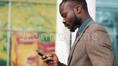 快乐的非裔美国人在商务中心附近的街道上，在他的智能<strong>手机</strong>上<strong>输入</strong>一条信息。 概念