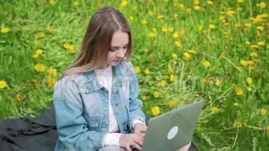 女人坐在公园的绿草上，带着笔记本电脑，笔记本电脑。 学生在户外学习