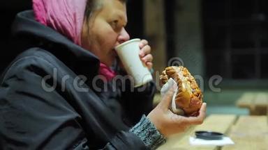 饥饿的成年妇女在慈善活动中喝茶和吃热狗，快餐