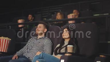 一个年轻人和一个朋友在电影院看电影，并且嘲笑他们在屏幕上看到的东西