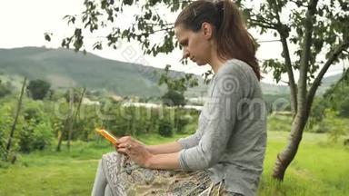 4k灰色女孩在绿色的田野、山丘、棕榈园、木头和手的农村背景下<strong>输入</strong>智能<strong>手机</strong>