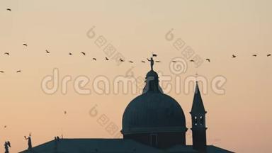 一群鸟飞过粉红色的夕阳天空。 历史建筑的背景