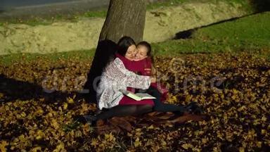 妈妈和女儿坐在树下看书。他们说得很好。妈妈和女儿在秋林里。他们是