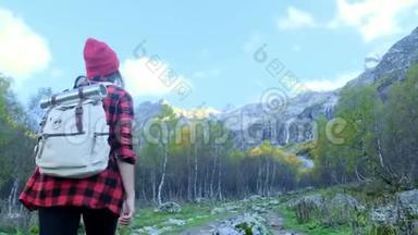 活跃的年轻时髦女孩穿过树林，沿着山间的小路走。 她戴着一顶红帽子
