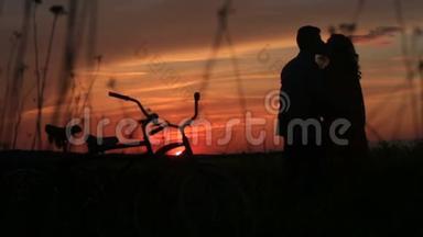 在田野的夕阳下，这对温柔相爱的夫妇的剪影轻轻地亲吻着红色明亮的天空。 散步与散步
