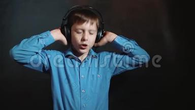 耳机小男孩在黑色背景下听音乐工作室。 年轻的金发欧洲德国男孩戴着耳机摇着