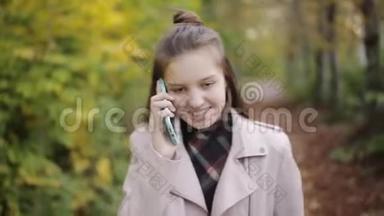 少女在公园里散步，在手机，智能手机上聊天。 秋天的天气，黄叶和凉爽