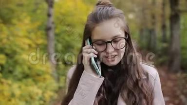 少女在公园里散步，在手机，智能手机上聊天。 秋天的天气，黄叶和凉爽