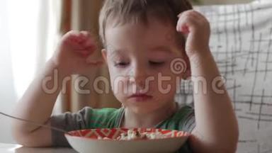 可爱的小宝宝一个人用勺子从盘子里吃粥，健康饮食的概念。