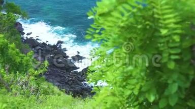 在绿色植物背景下，海浪飞溅到岩石海滩。 汹涌的海浪以泡沫和