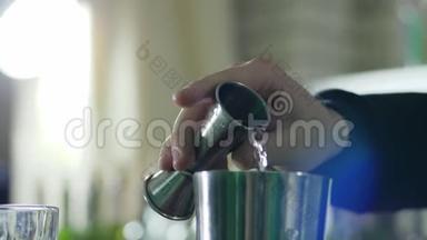 人的手握着跳汰机，在没有聚焦的背景上缓慢地将液体倒入金属杯中