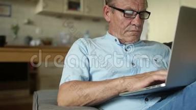 老人坐在沙发上从家里远程工作。 异地就业，为养老金领取者就业.. 退役旧笔记本电脑